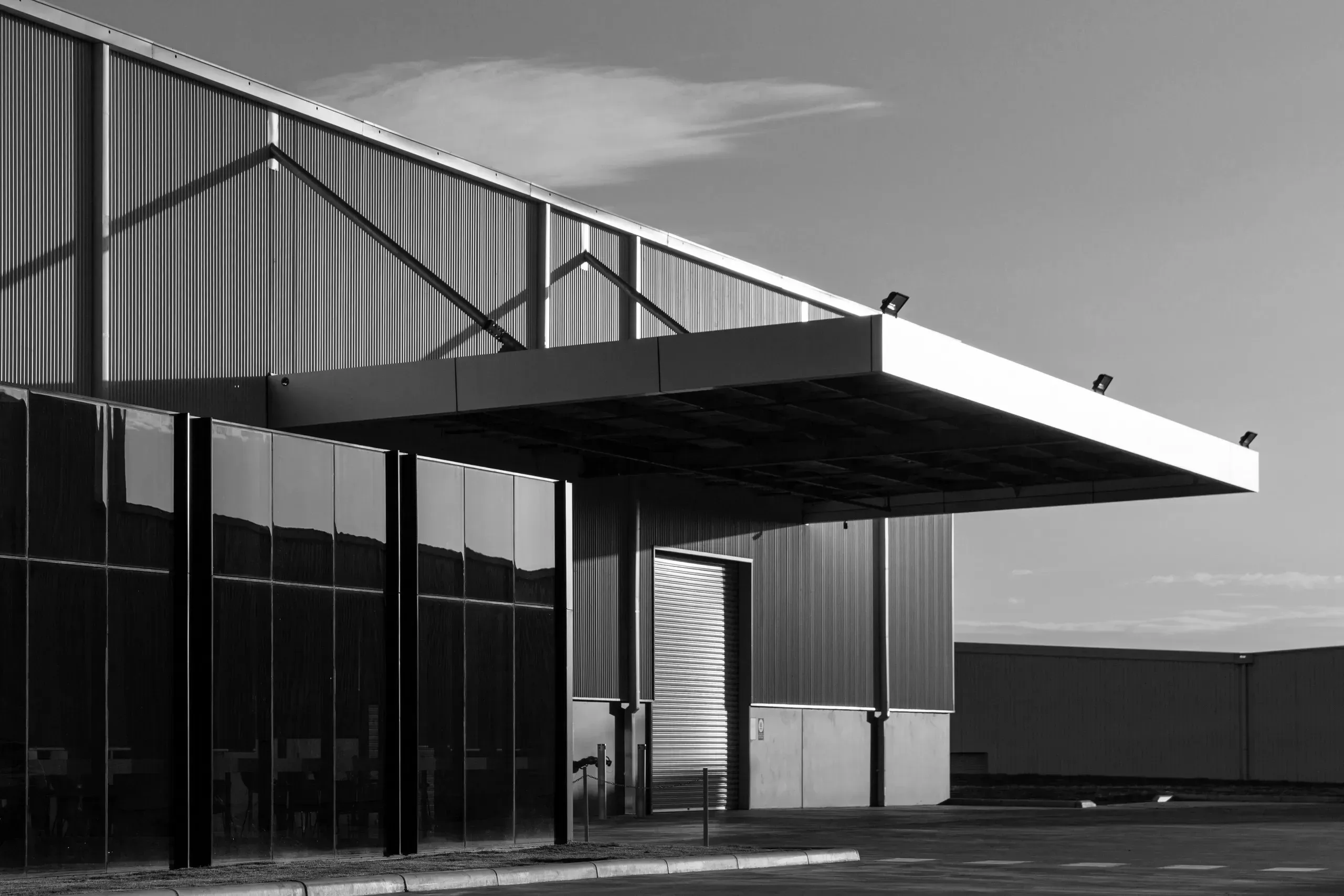 Modern industrial building with black corrugated metal siding and cantilevered awning in black and white photography.