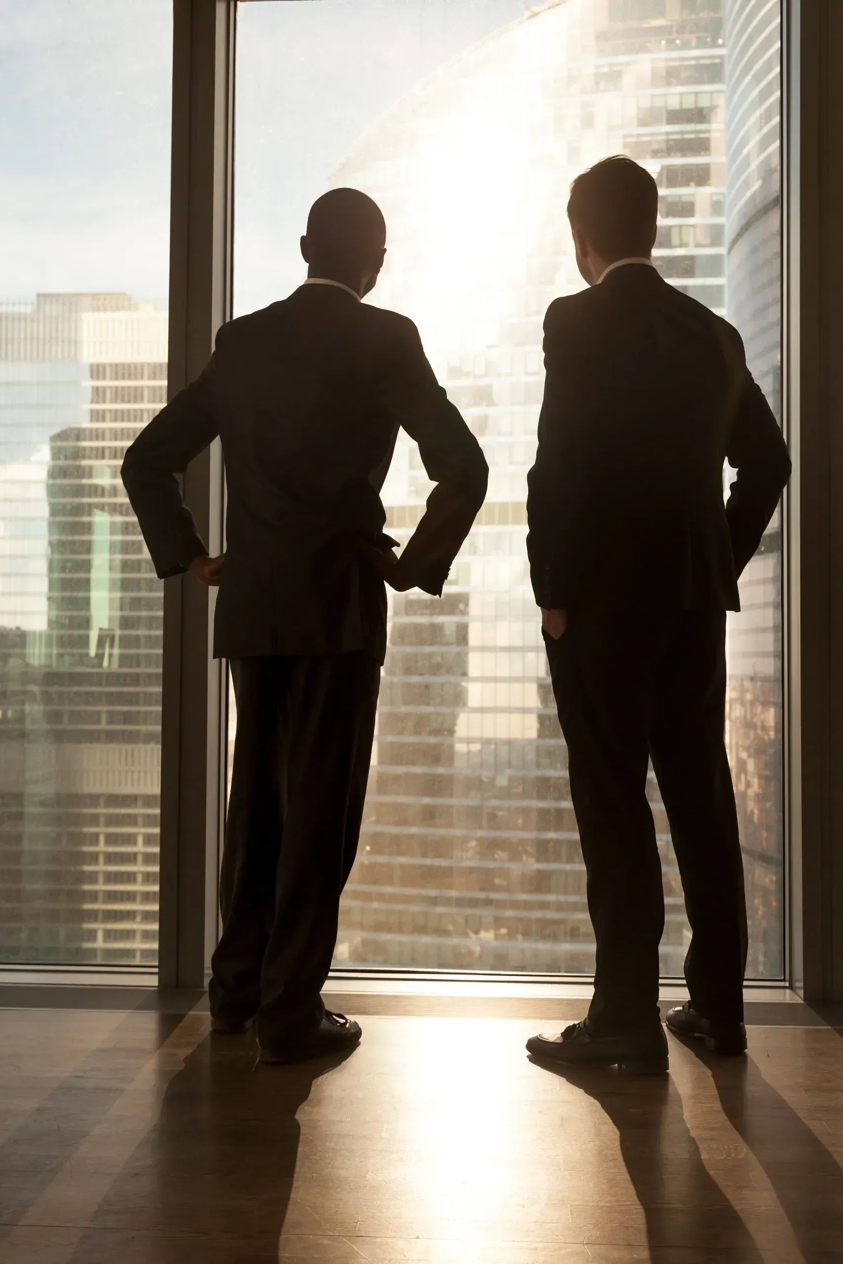 Two businessmen in suits viewing city skyline from high-rise office window
