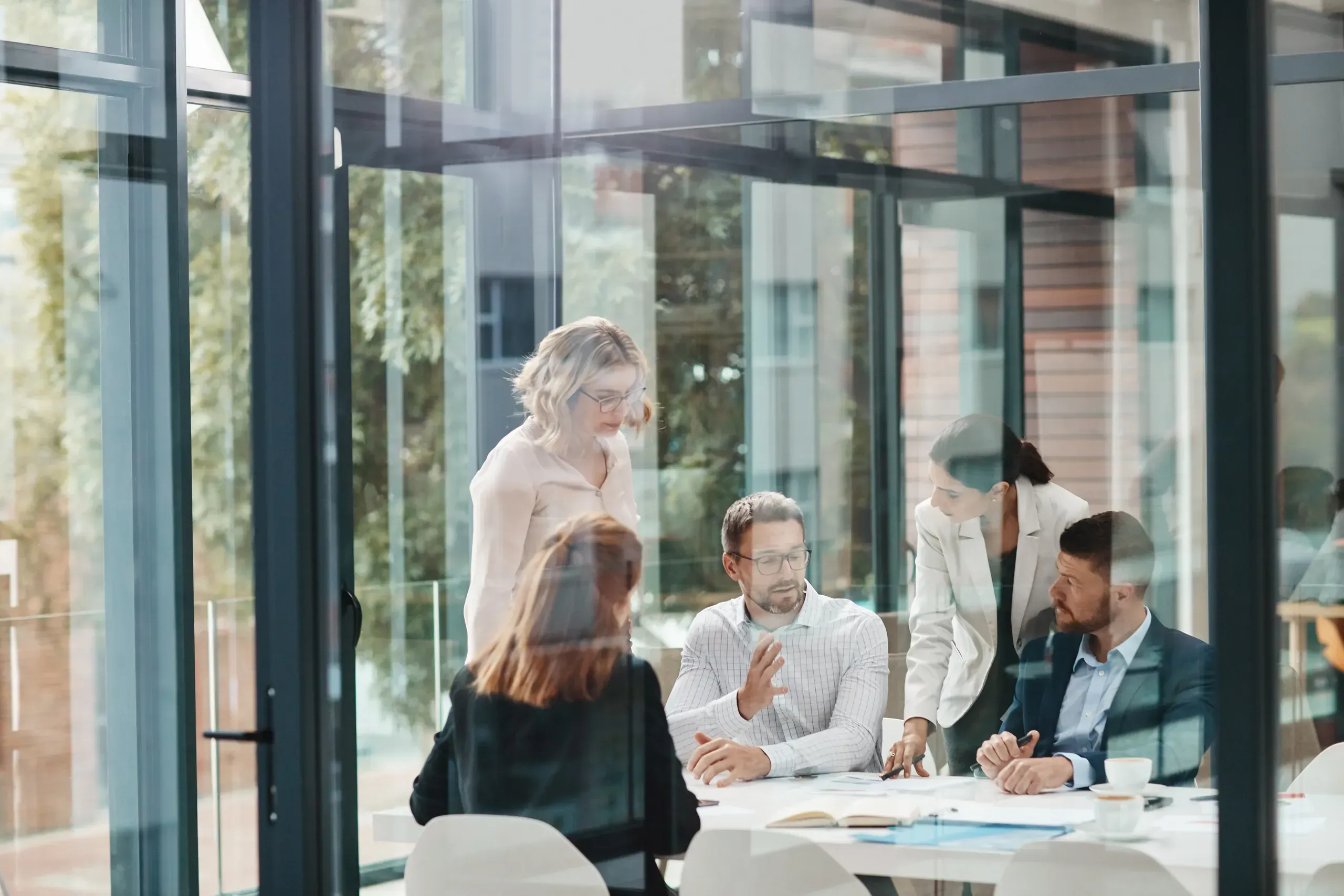 Professional business meeting in modern office with glass walls and multiple employees discussing documents