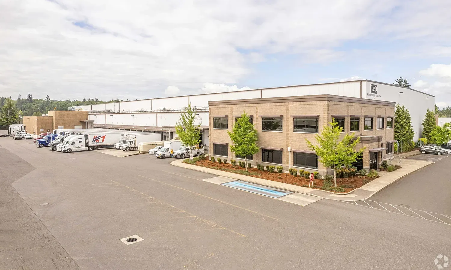 Modern industrial warehouse building with brick facade and large parking lot with vehicles parked outside