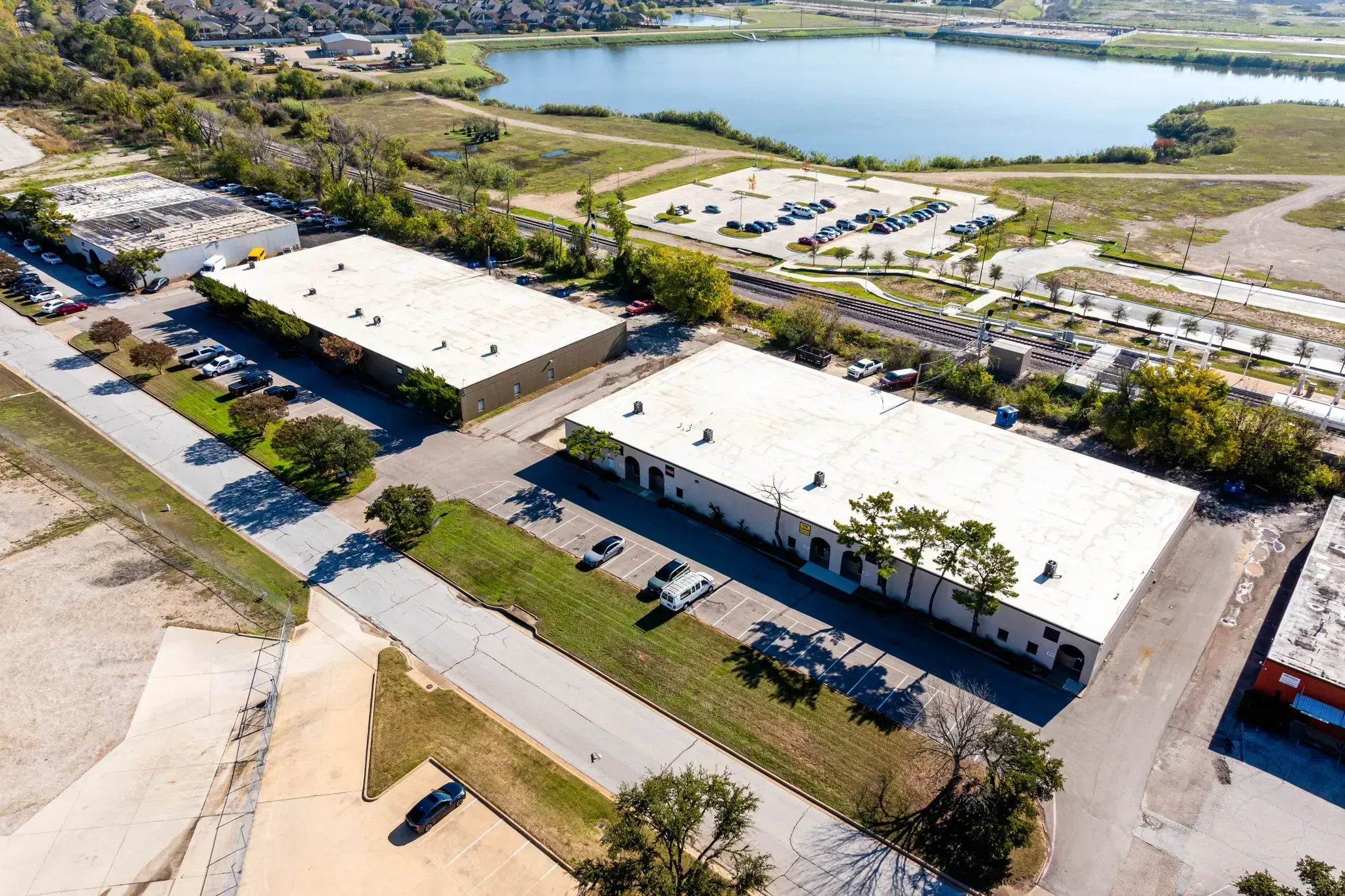 Aerial view of industrial warehouse buildings with parking lots near a waterway and green fields.