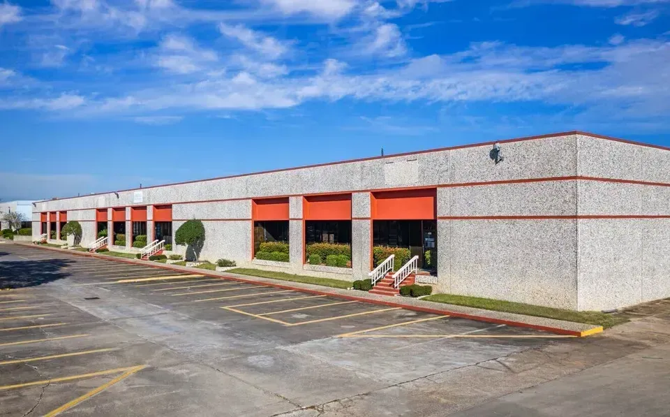 Commercial building with red overhead doors, concrete facade, and parking lot under blue sky