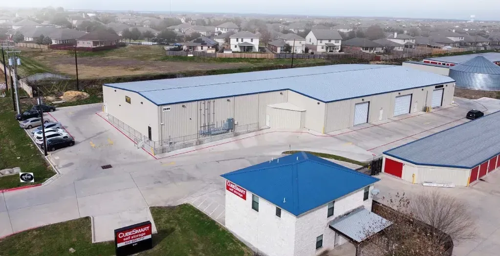 Commercial industrial complex with large warehouse buildings and blue roof structure in residential area